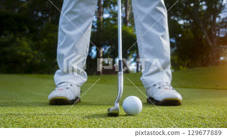 Golfer putting ball on the green golf, lens flare on sun set evening time. Golfer hitting golf ball. 129677889