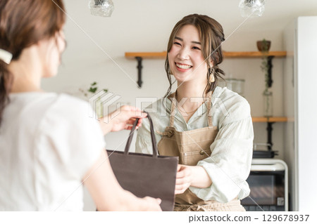 A female cafe attendant handing out takeaway items to customers at a cafe or restaurant A female cafe attendant handing out takeaway items to customers at a cafe or restaurant 129678937