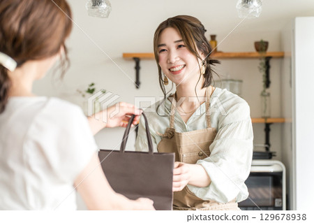A female cafe attendant handing out takeaway items to customers at a cafe or restaurant A female cafe attendant handing out takeaway items to customers at a cafe or restaurant 129678938