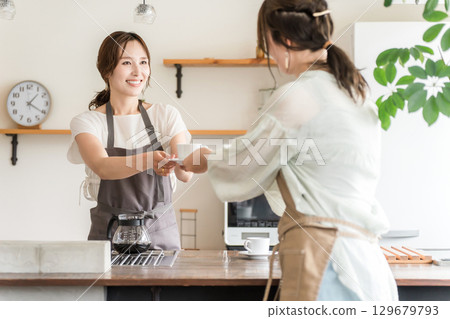 Asian female cafe attendant wearing an apron handing over a coffee cup from the kitchen counter Asian female cafe attendant wearing an apron handing over a coffee cup from the kitchen counter 129679793