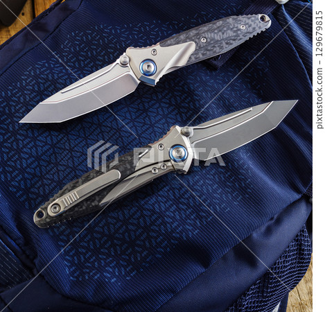 Folding EDC knife with pocket clip in open and closed position on blue background. 129679815