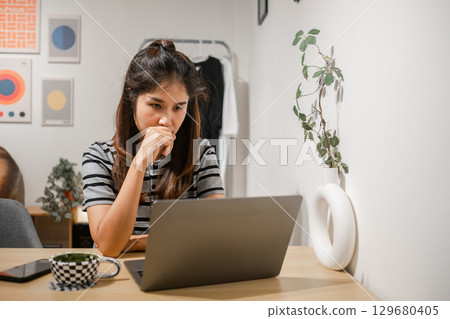 A young woman concentrating on her laptop in a stylish home office with modern decor and minimalist design. A young woman concentrating on her laptop in a stylish home office with modern decor and minimalist design. 129680405