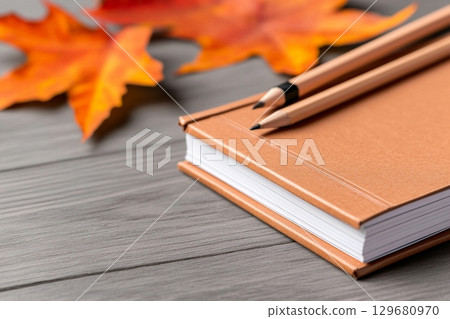 Notebook with pencils placed on a wooden table, surrounded by autumn leaves. 129680970