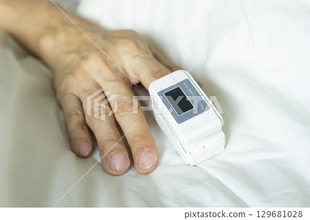Cropped view of male patient using oximeter on finger lying in bed. 129681028