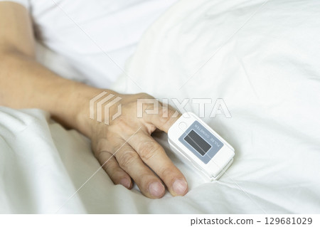 Cropped view of male patient using oximeter on finger lying in bed. 129681029