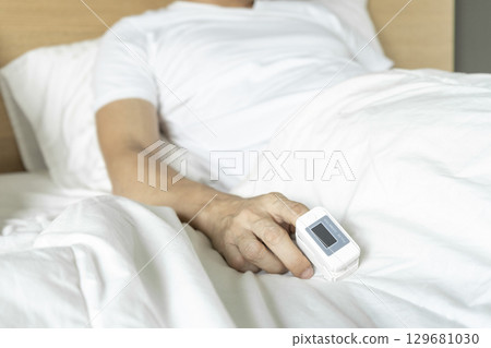 Cropped view of male patient using oximeter on finger lying in bed. 129681030