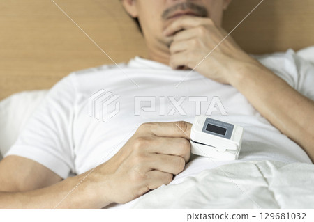 Cropped view of male patient using oximeter on finger lying in bed. Cropped view of male patient using oximeter on finger lying in bed. 129681032