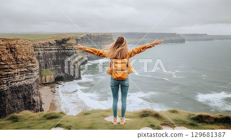 Woman Embraces Freedom on Cliffs of Moher, Arms Outstretched, Wi Woman Embraces Freedom on Cliffs of Moher, Arms Outstretched, Wi 129681387