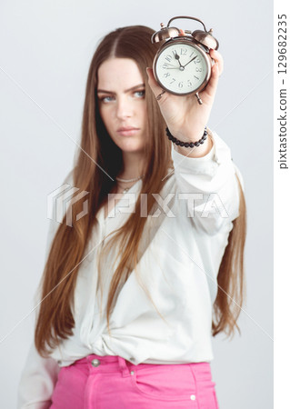 Woman with serious face showing retro clock Woman with serious face showing retro clock 129682235