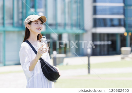 A woman wearing a cap hydrating outdoors 129682400