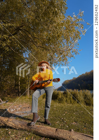 Blonde woman playing string guitar outdoors in autumn forest. Concept of sound therapy, mental health and wellness rituals. Calmness tranquility audio-sensory practices. Aura farming energy Blonde woman playing string guitar outdoors in autumn forest. Concept of sound therapy, mental health and wellness rituals. Calmness tranquility audio-sensory practices. Aura farming energy 129682492