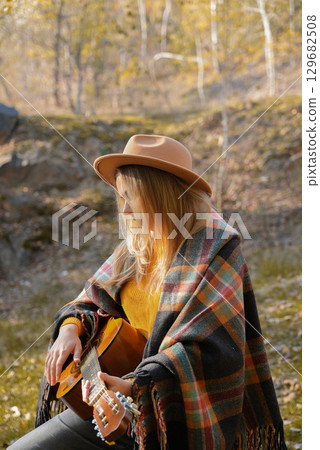 Portrait of smiling caucasian artist plays wooden acoustic guitar in autumnal park. Young songwriter plays string musical instrument hobby outside in nature fall time. Audio music healing 129682508