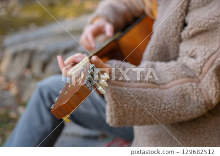 Close up of hands playing string guitar outdoors in autumn forest. Concept of sound therapy, mental health and wellness rituals. Calmness tranquility audio-sensory practices. Aura farming energy Close up of hands playing string guitar outdoors in autumn forest. Concept of sound therapy, mental health and wellness rituals. Calmness tranquility audio-sensory practices. Aura farming energy 129682512