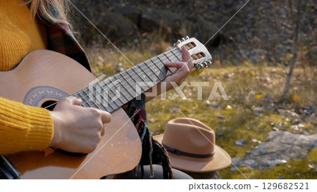 Close up of hands artist plays wooden acoustic guitar in autumnal park. Young songwriter plays string musical instrument hobby outside in nature fall time. Audio music healing 129682521