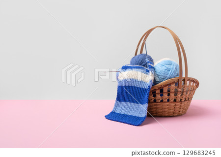 Blue and white knitting balls in basket with knitting needles and knitted scarf on pink background. Set for the hobby of knitting warm clothes or toys. Concept needlework Blue and white knitting balls in basket with knitting needles and knitted scarf on pink background. Set for the hobby of knitting warm clothes or toys. Concept needlework 129683245