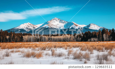 Landscape background wallpaper Majestic snow capped mountains rise under clear blue sky, surrounded by golden grassland and evergreen trees, creating serene winter landscape 129683511