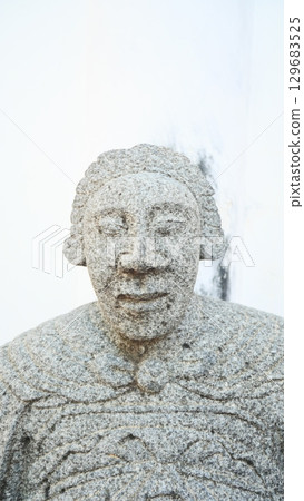 Close-up of a weathered stone statue head with a peaceful expression Close-up of a weathered stone statue head with a peaceful expression 129683525