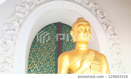 A golden Buddha statue in a white ornate alcove at a temple in Thailand A golden Buddha statue in a white ornate alcove at a temple in Thailand 129683526