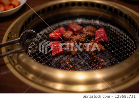 Close-up of meat grilling on a Korean barbecue grill with tongs 129683731