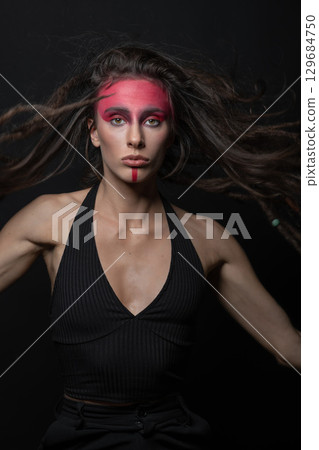 Model with tribe red paint make-up and hair with dreadlocks jumping in air and looking at camera 129684750