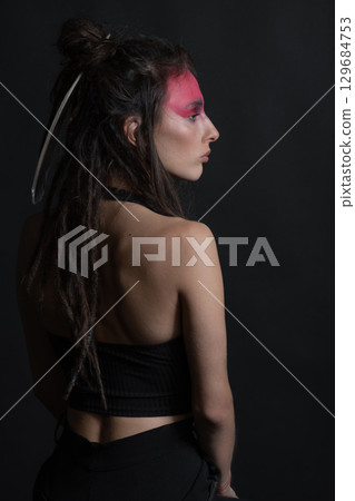 Studio portrait of woman with red Indian tribe make-up, dreadlocks and feather in hair Studio portrait of woman with red Indian tribe make-up, dreadlocks and feather in hair 129684753