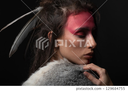 Studio portrait of woman with red Indian tribe make-up, dreadlocks and feathers in hair Studio portrait of woman with red Indian tribe make-up, dreadlocks and feathers in hair 129684755