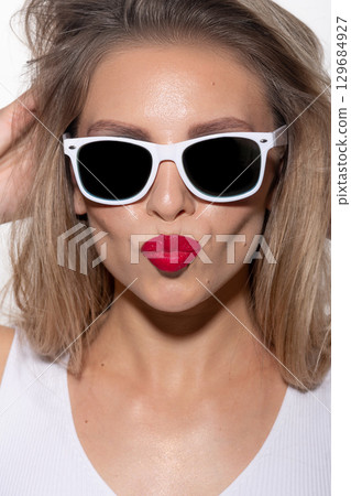 Beautiful woman close-up studio portrait with white sunglasses and red lipstick sending kiss Beautiful woman close-up studio portrait with white sunglasses and red lipstick sending kiss 129684927