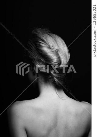 Studio portrait of beautiful woman standing back to camera with hair bun hairstyle 129685021