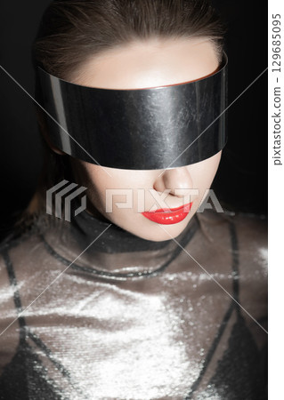 Abstract woman studio portrait with make-up and metallic glasses or helmet covering her eyes 129685095