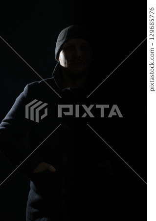 Man with coat and hat hiding in shadow and silhouette illuminate with light 129685776
