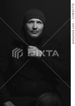 Serious man with black winter coat and winter hat studio portrait Serious man with black winter coat and winter hat studio portrait 129685778