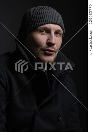 Serious man with black winter coat and winter hat studio portrait Serious man with black winter coat and winter hat studio portrait 129685779