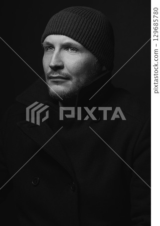 Serious man with black winter coat and winter hat studio portrait 129685780