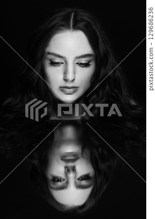 Portrait of beautiful woman with wavy hair and face reflection in mirror Portrait of beautiful woman with wavy hair and face reflection in mirror 129686236