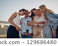Friends joyfully sharing smartphone moments outdoors, enjoying life and each other together 129686480