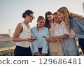 A lively group of five diverse women, engaged with their smartphones and enjoying the outdoors 129686481