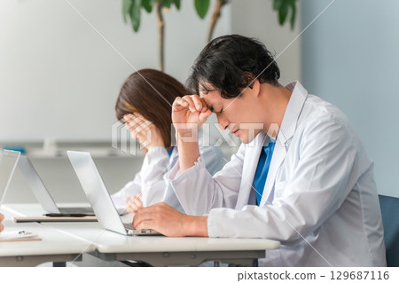 Overwork, fatigued male doctor holding his head, doctor (poor health, lack of sleep, doctor shortage, stress) Overwork, fatigued male doctor holding his head, doctor (poor health, lack of sleep, doctor shortage, stress) 129687116
