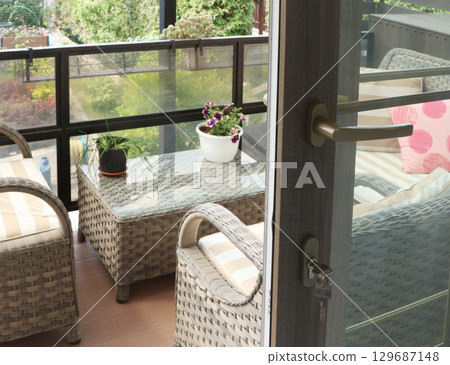 Wicker furniture on a wooden terrace on a sunny summer day. Open modern sliding door. Leisure and lifestyle. 129687148