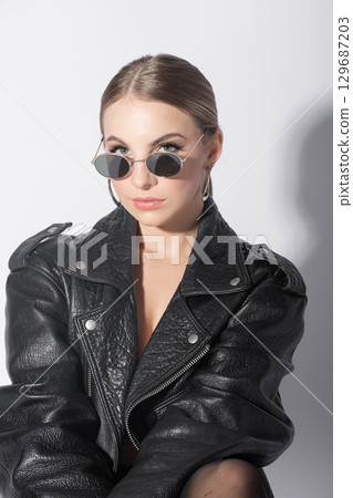 Woman studio portrait with black punk leather jacket, sunglasses and without bra 129687203