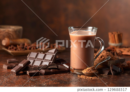 Pieces of bitter chocolate and glass of cocoa drink on a brown table. 129688317