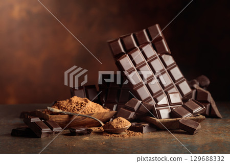 Scraps of dark chocolate next to a wooden bowl of cocoa powder. Scraps of dark chocolate next to a wooden bowl of cocoa powder. 129688332