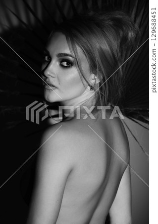 Beautiful woman with naked back and palm leaf black and white studio portrait Beautiful woman with naked back and palm leaf black and white studio portrait 129688451