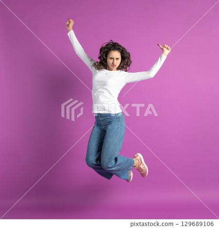 Positive young girl jumping in air against purple background Positive young girl jumping in air against purple background 129689106