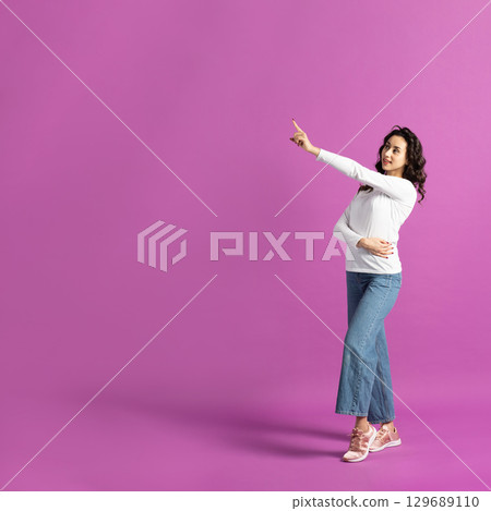 Woman pointing with finger to blank zone on purple background 129689110