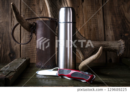 Hunting photo with a knife and a thermos. Knife and thermos against the background of a moose mountain. Hunting photo with a knife and a thermos. Knife and thermos against the background of a moose mountain. 129689225