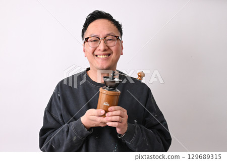 Middle-aged man smiling while holding a coffee grinder 129689315
