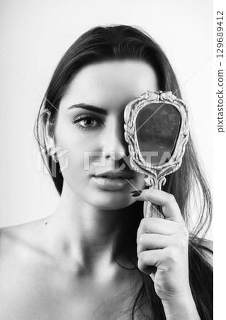 Beautiful woman covers her one eye with old mirror 129689412