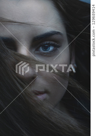 Beautiful woman with blue eyes cover her face with hair 129689414