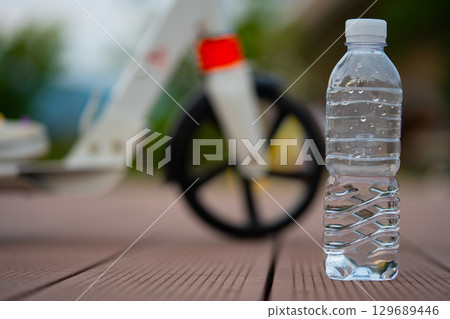 A bottle of clean water and a scooter wheel. After exercise on a summer evening. A bottle of clean water and a scooter wheel. After exercise on a summer evening. 129689446