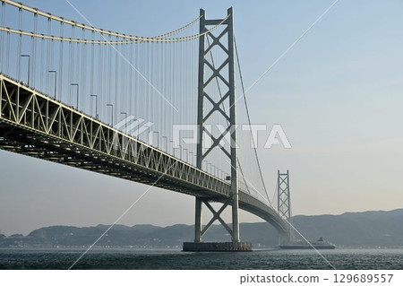 A distant view of a cruise ship passing through the Akashi Kaikyo Bridge from the Bridge Science Museum in Maiko Park 129689557